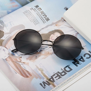 Vintage round sunglasses with black metal frame and dark lenses on a magazine backdrop