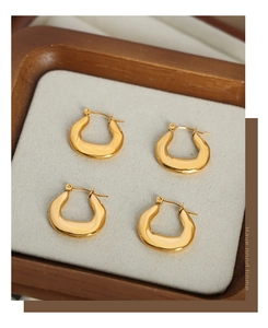 Detailed top view of gold geometric hoop earrings on a beige velvet jewelry tray
