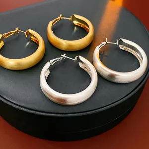 Brushed gold and silver hoop earrings on a black display with matte texture finish