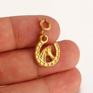 Macro view of a 18K gold-plated horseshoe pendant with horse head detail held in hand
