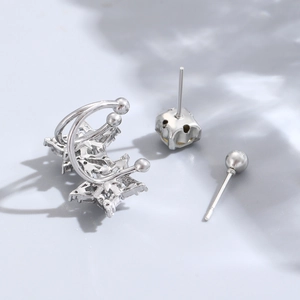 Macro shot of silver star-shaped ear cuff and zircon stud earrings set on gray background