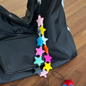 Colorful star bead phone strap attached to a black backpack on a natural wooden floor