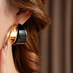 Close-up of a model wearing C-shaped black and gold plated resin hoop earrings