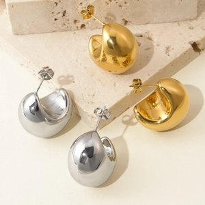 Detailed close-up of chunky gold and silver teardrop earrings on a textured stone base