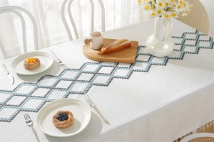 Close-up of light gray waterproof tablecloth with blue geometric diamond embroidery and tassels