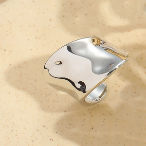 Macro shot of silver adjustable organic ring with polished mirror finish on sandy background