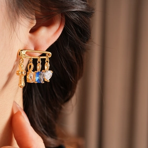 Close-up of gold paperclip drop earring with cross, blue stone and heart zircon