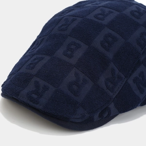 Close-up of navy blue flat cap featuring embossed letter R textured terry cloth fabric