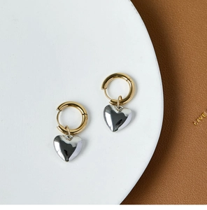 Close-up of gold hoop earrings with silver heart charms on a leather and ceramic base