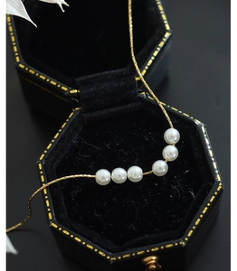 Detailed view of six white pearls on a gold-plated titanium steel necklace in a gift box