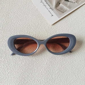 Detail view of oval blue resin sunglasses with brown gradient lenses on a white textured background