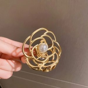 Detail of a golden camellia hair claw clip with a large pearl centerpiece and hollow design