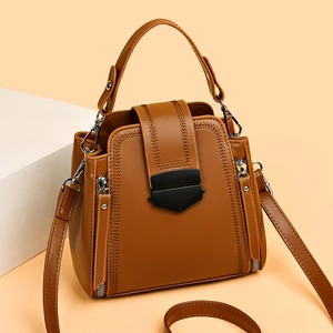 Brown leather crossbody handbag with black hardware and detachable strap on beige background