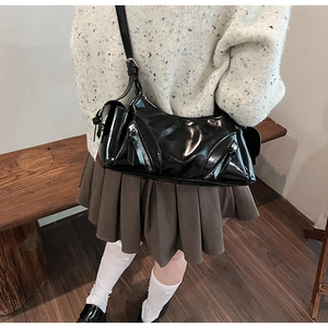 Close-up of a black patent leather shoulder bag worn by a model in a minimalist setting