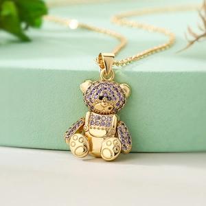 18K gold plated teddy bear pendant necklace with purple zircons on a green pedestal