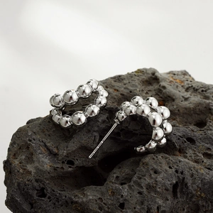 Polished silver beaded C-shaped hoop earrings on black volcanic rock display