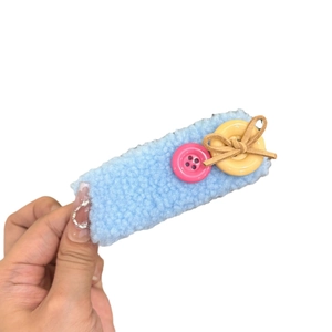 Blue teddy fur hair clip with pink and yellow button bow detail held in hand
