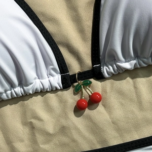 Close-up of bikini top with black trim and decorative cherry pendant on fabric