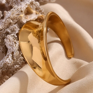 Detail view of gold wave concave open bangle on beige fabric and natural porous rock