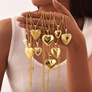 Close-up of golden heart lockets with love engraving and floral patterns held by a hand