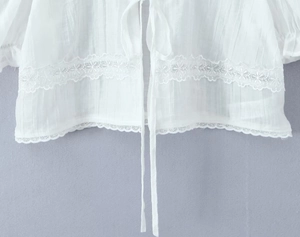 Détail du haut blanc à nouer avec bordure en dentelle et tissu à rayures verticales