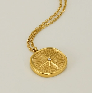 Macro shot of 18k gold plated starburst medallion necklace with a central sparkling zircon