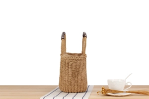 Detail of hand-woven straw bag featuring dual handles and a beige drawstring fabric liner