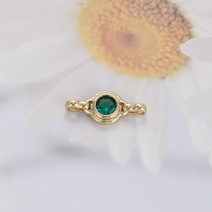 Detailed close-up of emerald green zircon gold bracelet link on elegant floral texture