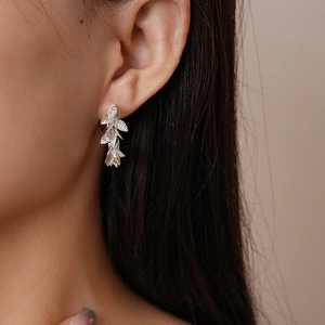 Gros plan de boucles d'oreilles en feuilles argentées portées avec un éclairage doux