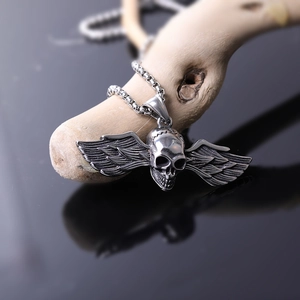Macro shot of stainless steel winged skull pendant on wooden surface with metal chain