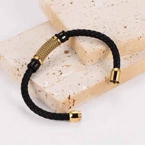 Braided black leather bracelet with golden metal accents on beige stones display