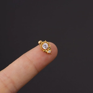Makroaufnahme eines goldenen Edelstahl-Ohrsteckers mit klaren Zirkon-Kristallen am Finger