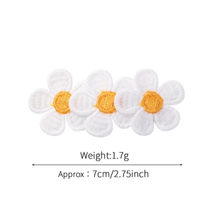 Détails de trois écussons brodés de marguerites blanches avec cœur jaune sur fond blanc