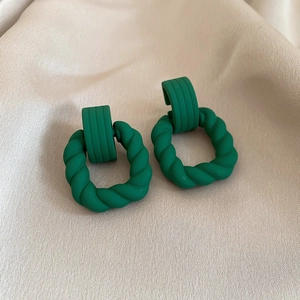 Detail of dark green geometric earrings with matte finish on beige silk fabric