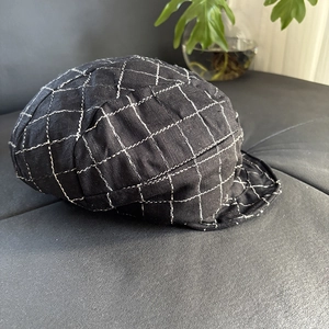 Close-up of black plaid baker boy hat with white stitched grid pattern on grey fabric