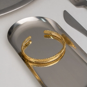 Detailed close-up of 18K gold-plated braided cuff bangle on an elegant metal tray