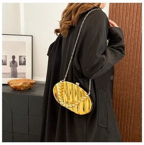 Detail of a gold metallic evening shell clutch bag with wavy texture on a black coat