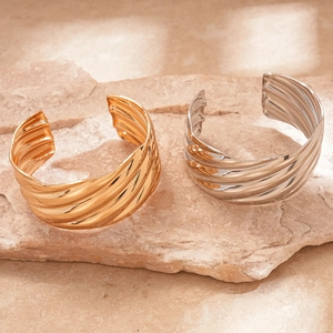 Polished wavy geometric open cuff bracelets in gold and silver finish on a natural stone base