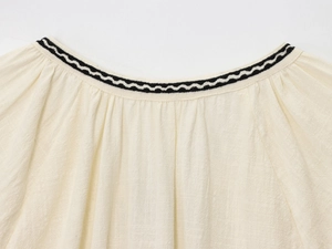 Détail de l'encolure d'une chemise en coton crème avec bordure ondulée noire ric-rac