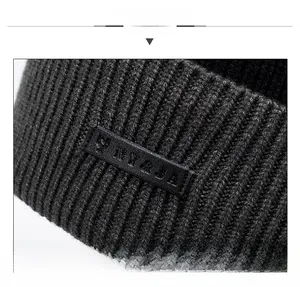Close-up of deep gray knit texture with embossed black leather logo patch on beanie