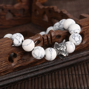 Detailed view of howlites bead bracelet with carved silver wolf head on wooden stand