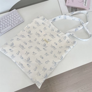 Close-up of white canvas tote bag with blue cat prints and center brand woven label