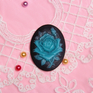 Macro detail of blue rose relief pendant on black base over pink lace fabric