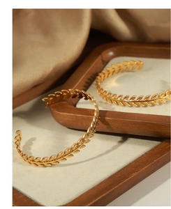Close-up of golden wheat leaf textured open cuff bracelet on a wooden display tray