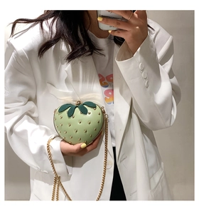 Detailed mirror selfie showing a light green strawberry shaped crossbody bag with gold studs