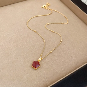 Macro shot of gold plated necklace with red enamel flower pendant on beige velvet tray