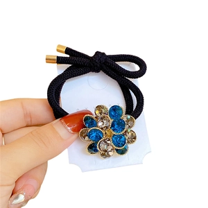 Elastic hair tie with blue crystal flower charm and gold accents on a white background