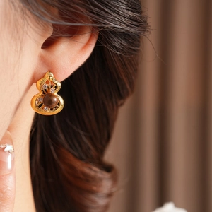 Close-up of vintage gourd earrings with tiger eye stone and pearls on a model's ear