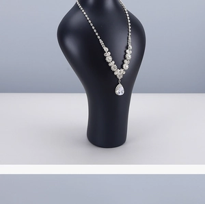 Macro shot of silver-tone necklace with teardrop pendant on black mannequin stand