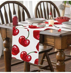 Linen table runner with red cherry print on wooden table in warm dining room setting